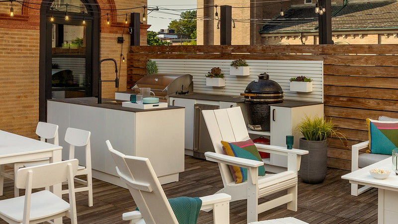 A rustic outdoor kitchen features white wooden cabinets, porcelain countertops, and a stainless steel gas grill.