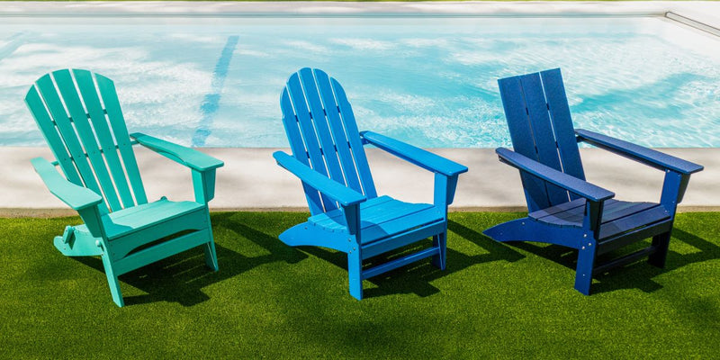 POLYWOOD Adirondack chairs in various shades of blue are styled in front of a swimming pool on a lawn.