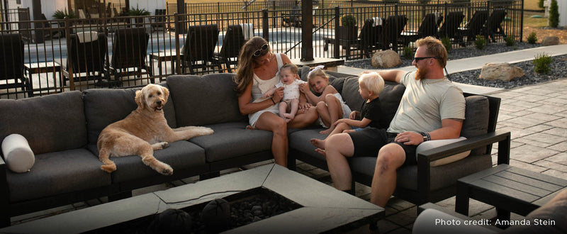 A family and their dog sit on a black POLYWOOD EDGE 6 Piece Modular Deep Seating Set with dark grey cushions by fire pit.