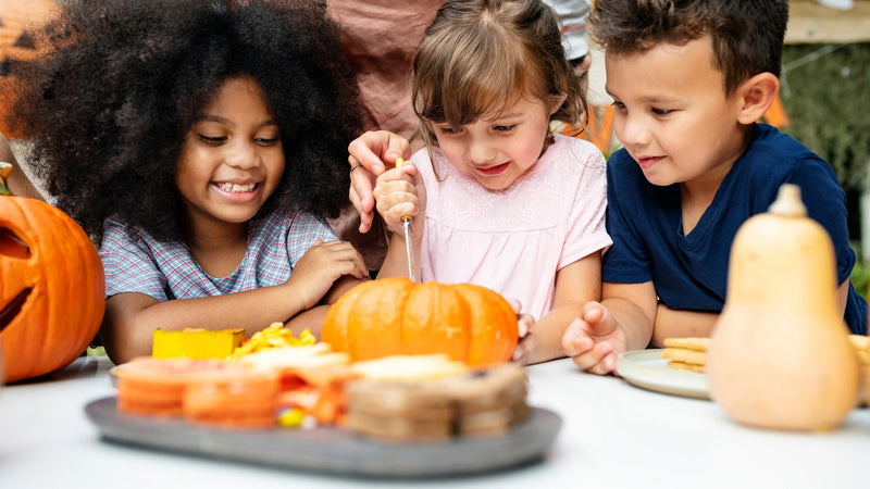 Kids sit at a table and carve pumpkins.