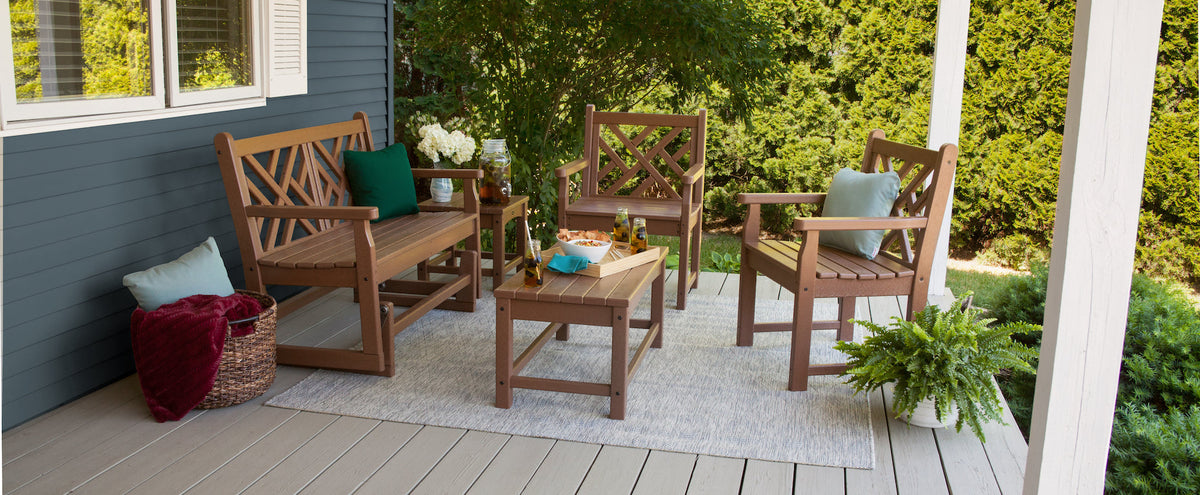 A POLYWOOD Chippendale 48 Inch Glider, Chippendale Garden Arm Chairs, a Club 18 Inch End Table, and a Club Coffee Table in Teak sit on a porch.