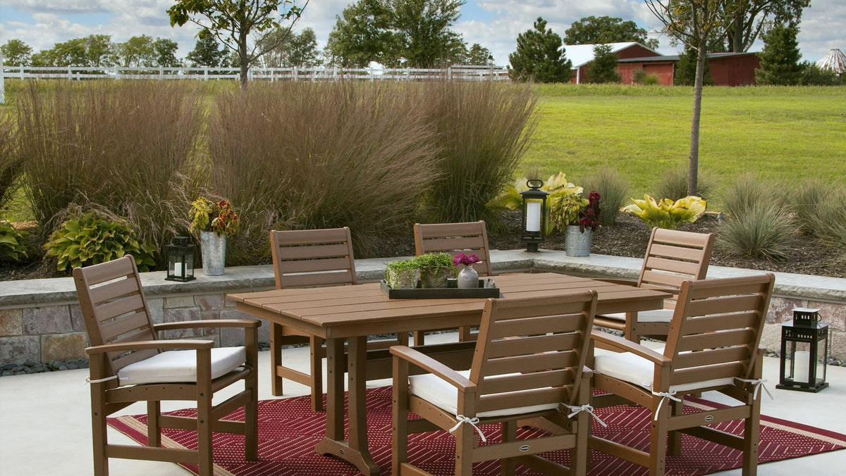 A POLYWOOD Signature 7 Piece Farmhouse Dining Set with Trestle Legs in Mahogany sits on a patio.
