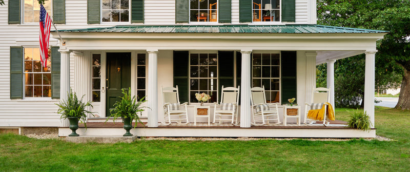 POLYWOOD Jefferson Woven Rocking Chairs in White with White Loom seats sit on a white house's wraparound porch.
