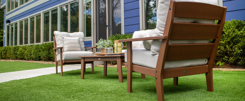 A brown POLYWOOD Lakeside 3 Piece Deep Seating Set with beige cushions sits on a lawn before a blue house with large windows.