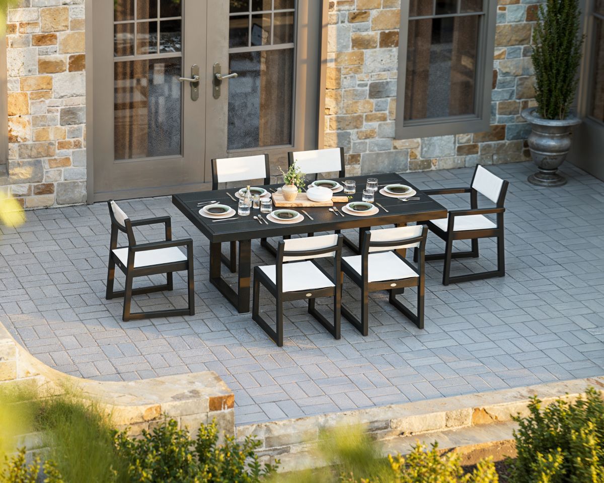 A POLYWOOD EDGE Sling 7 Piece Dining Set in Black with White Sling sits on a brick patio.