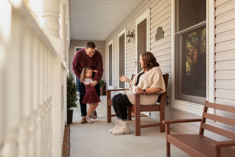 A man and a girl laugh while facing a smiling woman sitting on a POLYWOOD Lakeside 48 Inch Bench on a covered porch.