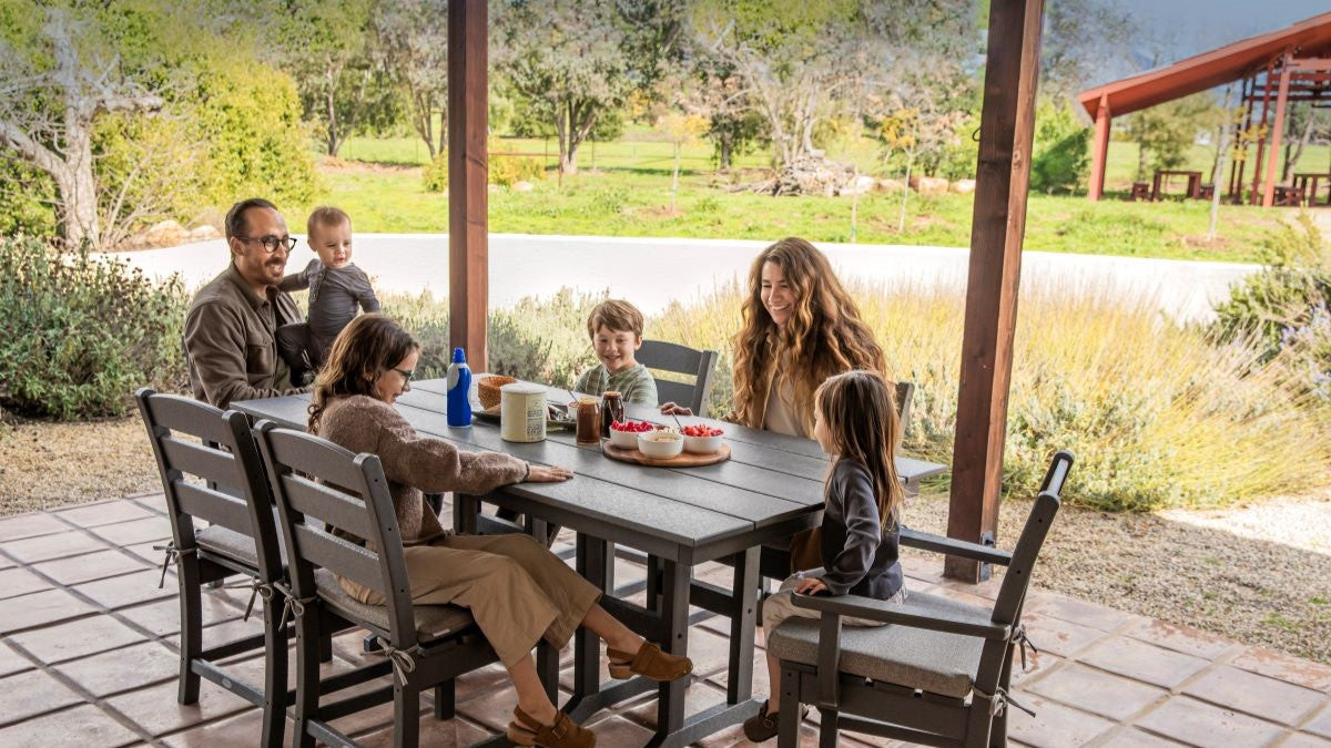 Family dining outdoors with a POLYWOOD® dining set on a sunlit patio, surrounded by greenery.