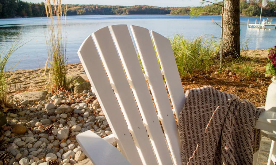 Close-up of a POLYWOOD Palm Coast adirondack chair, with a lakeside beach in the background, draped with a brown striped blanket.