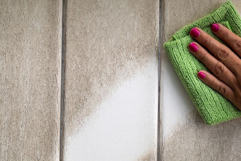 A hand with pink fingernails wiping down a white POLYWOOD outdoor bar cart with a green microfiber cloth, illustrating easy cleaning and maintenance.