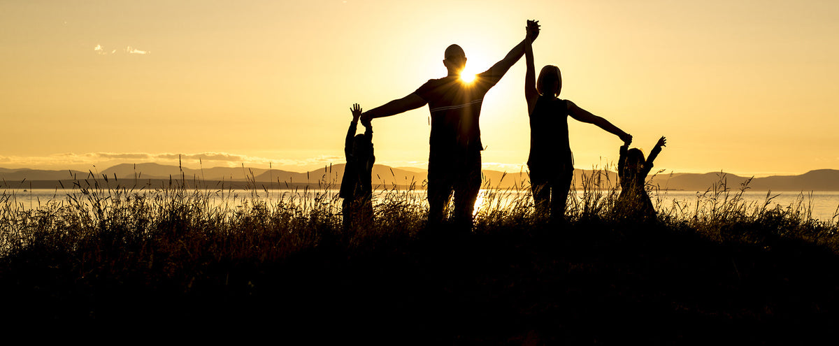 A family holds hands while standing on the grass before a lake at sunrise.