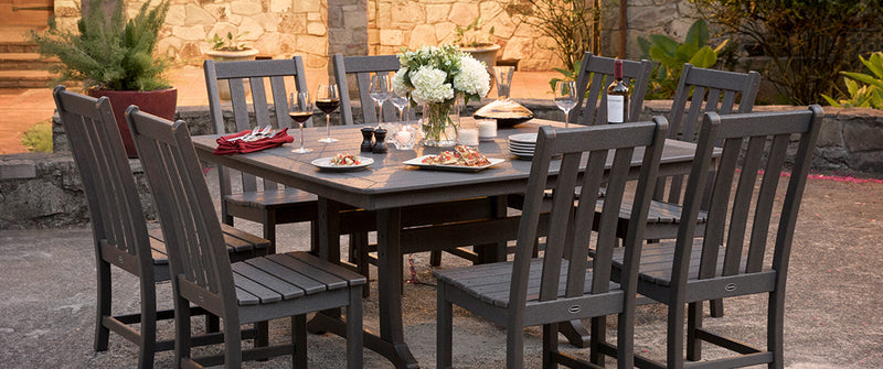 A POLYWOOD Vineyard 9 Piece Dining Set in Slate Grey is set for a meal on a concrete patio in front of a stone house.