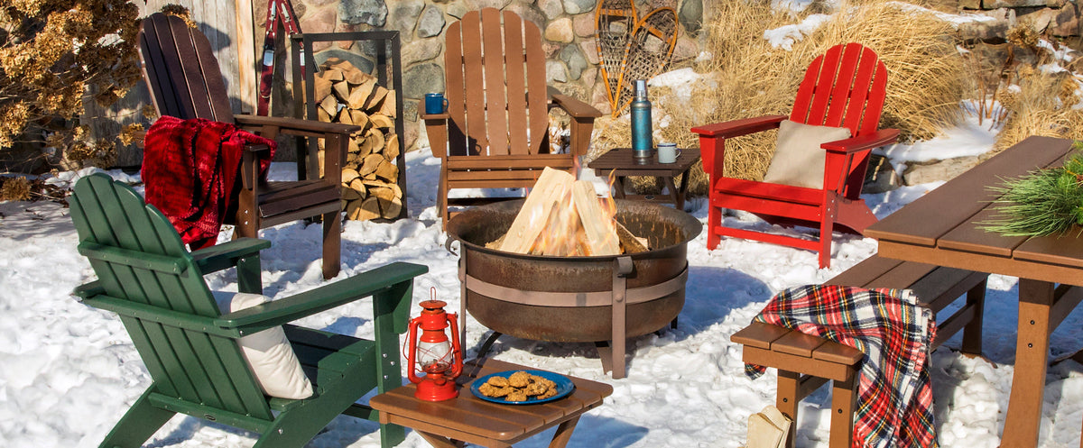 A snowy winter scene featuring an assortment of POLYWOOD seating and tables around a fire pit next to a stone cabin.