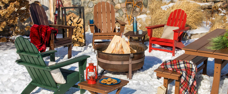 A snowy winter scene featuring an assortment of POLYWOOD seating and tables around a fire pit next to a stone cabin.
