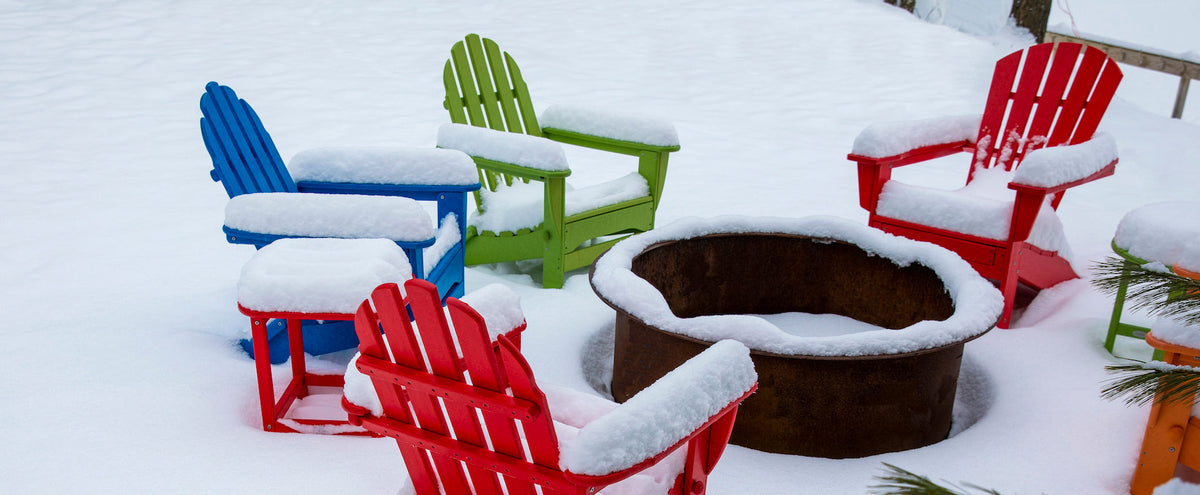 POLYWOOD Classic Folding Adirondack Chairs in Lime, Pacific Blue, and Sunset Red; a Seashell 18 Inch Side Table in Lime; and a Palm Coast Adirondack chair in Sunset Red encircle a fire pit in the snow.