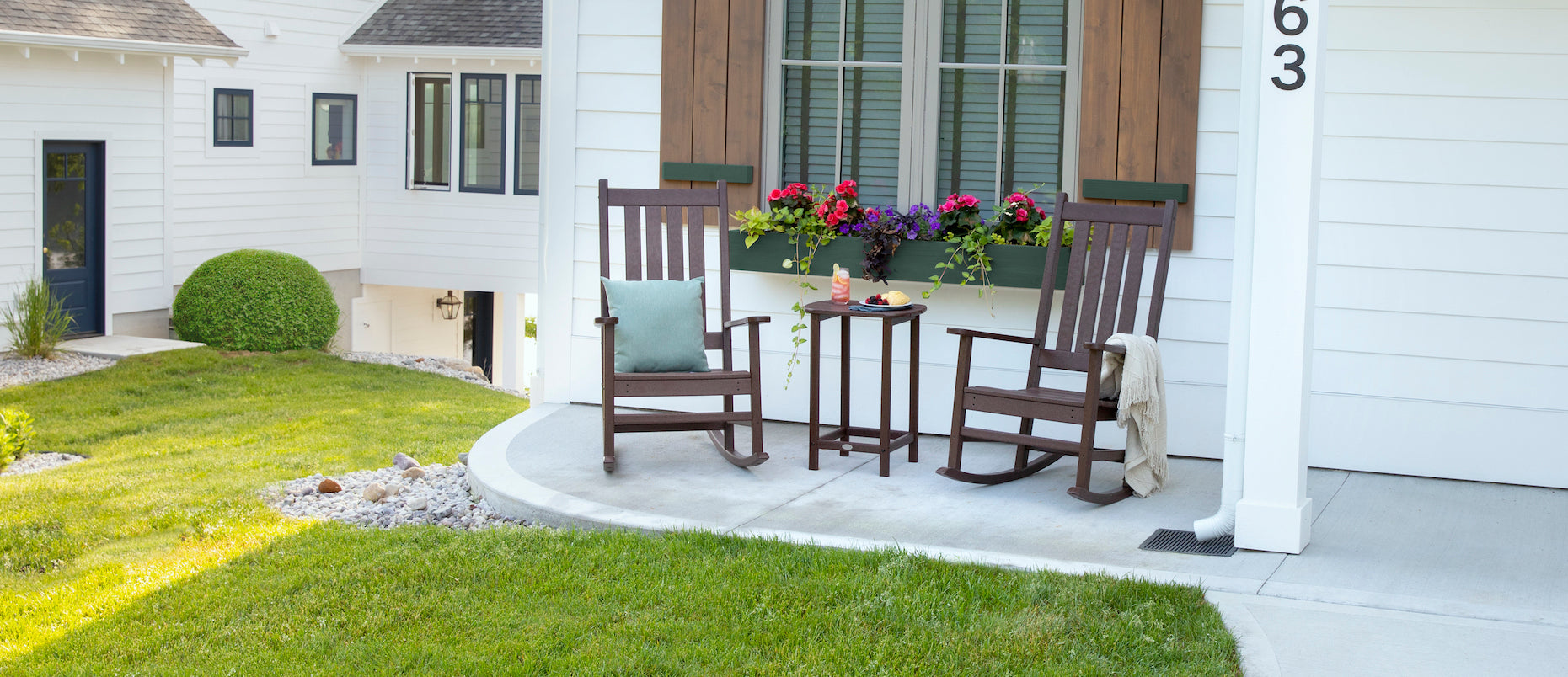 POLYWOOD Estate Rocking Chairs and a South Beach 26 Inch Counter Side Table sit on a concrete patio before a white house.