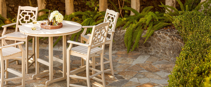 A tan POLYWOOD Chinoiserie 5 Piece Round Bar Set sits on a curved flagstone patio near a low stone wall covered in greenery.