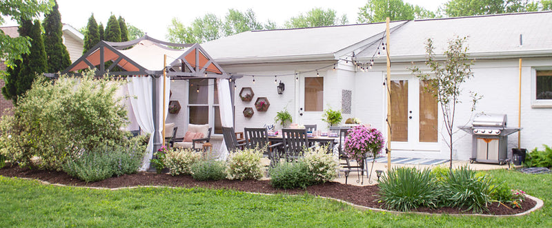 POLYWOOD dining and deep seating furniture, a pergola, string lights, and landscaping decorate a patio behind a brick house.