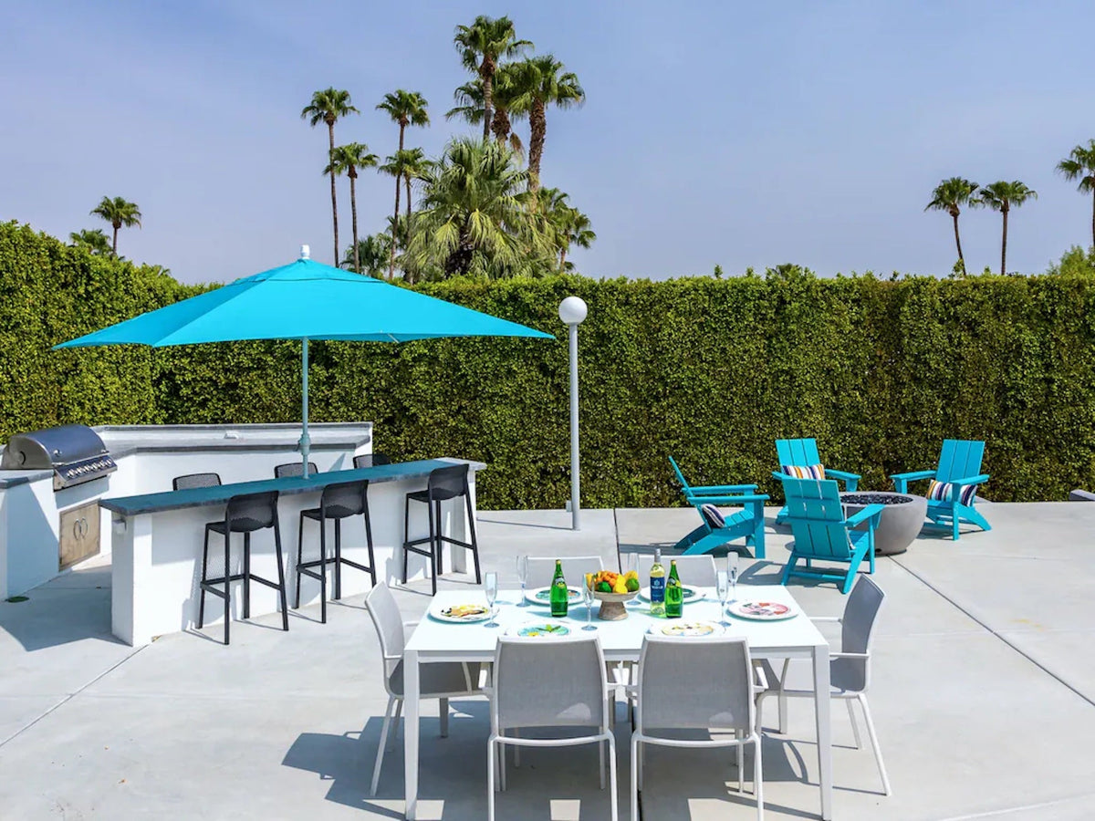 POLYWOOD Modern Adirondack Chairs in Aruba surround a fire pit next to an outdoor dining area surrounded by a tall hedge.