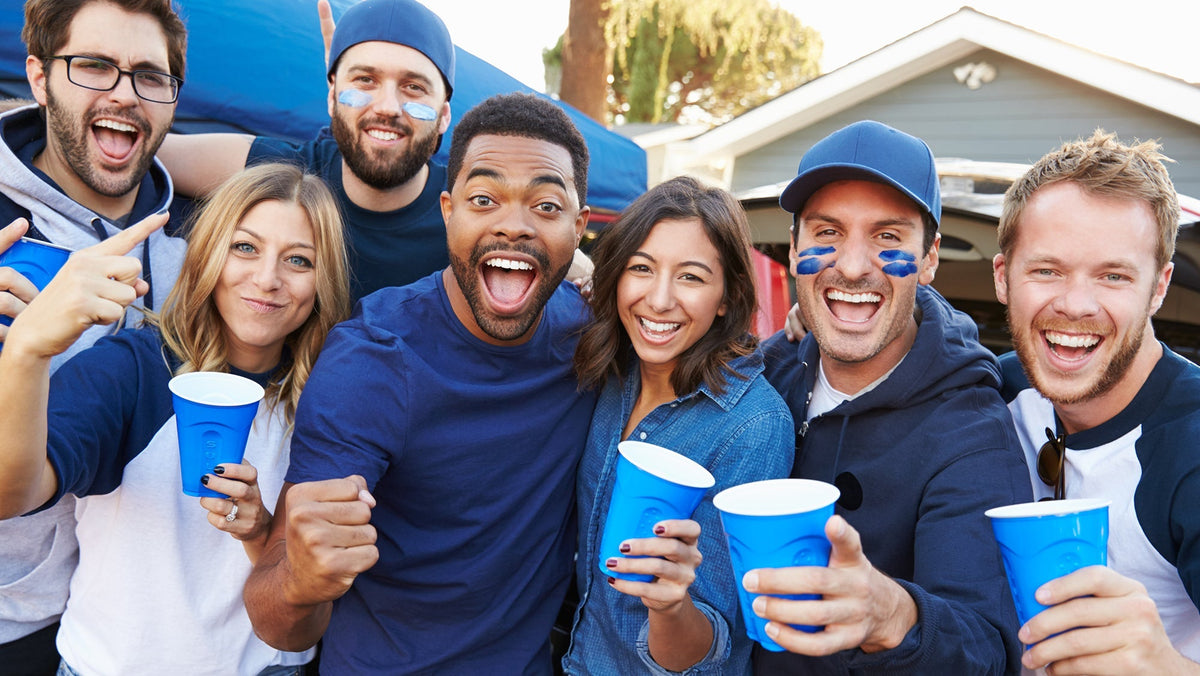 A group of friends wearing blue and white clothing smile and hold blue cups while celebrating outdoors.