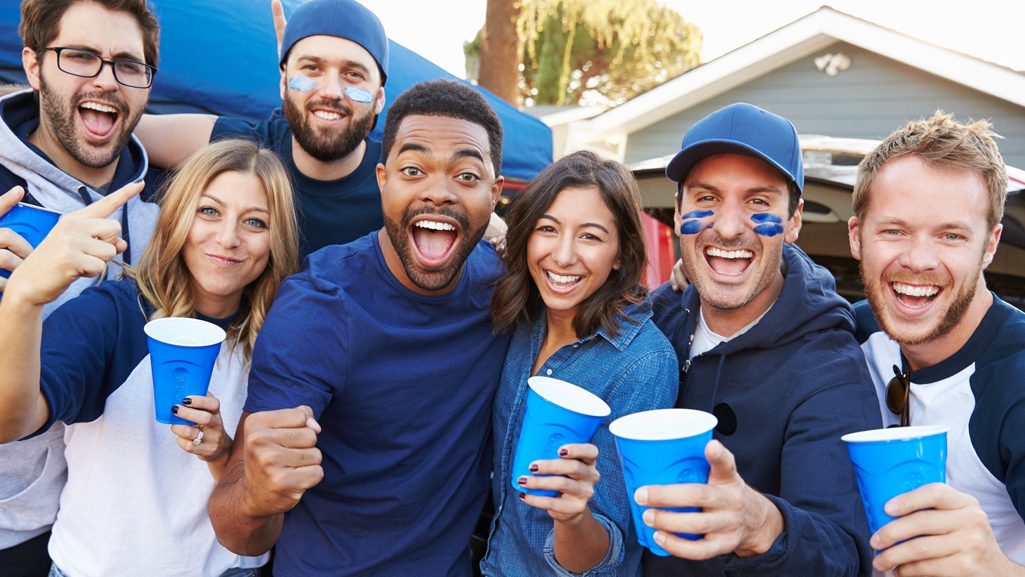 A group of friends wearing blue and white clothing smile and hold blue cups while celebrating outdoors.