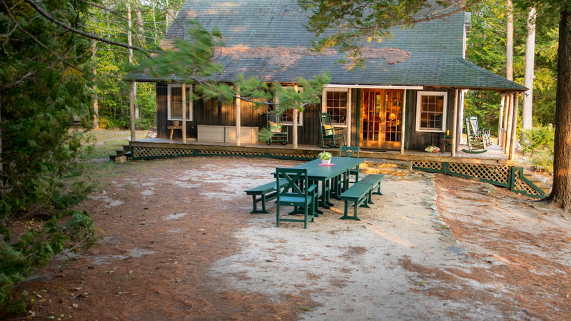 Assorted POLYWOOD dining furniture in Green sits by a cabin in the woods.