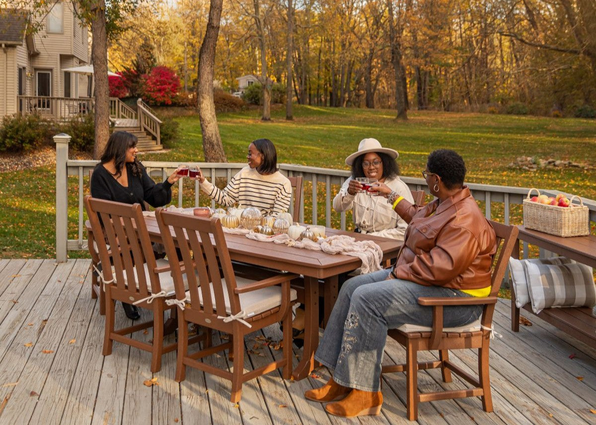 Women sitting at a brown POLYWOOD Vineyard 7 Piece Arm Chair Dining Set on a deck raise glasses in a toast to friendship.