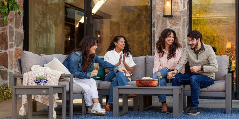 A group of friends sits on a grey POLYWOOD deep seating sectional, enjoying wine, popcorn, and each other's company.