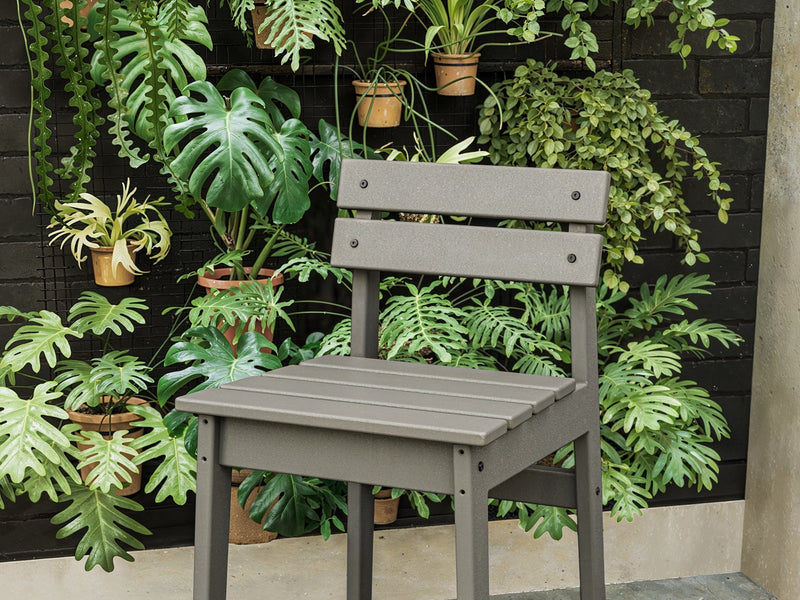 A grey POLYWOOD Modern Studio Plaza Lowback Counter Chair stands in front of a vertical garden with vibrant greenery.