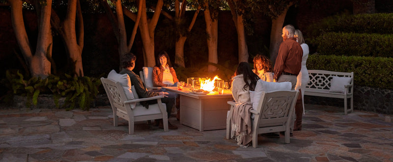 People sit and chat in POLYWOOD Chinoiserie Deep Seating Chairs by a Square 42 Inch Fire Pit Table on a stone patio at night.