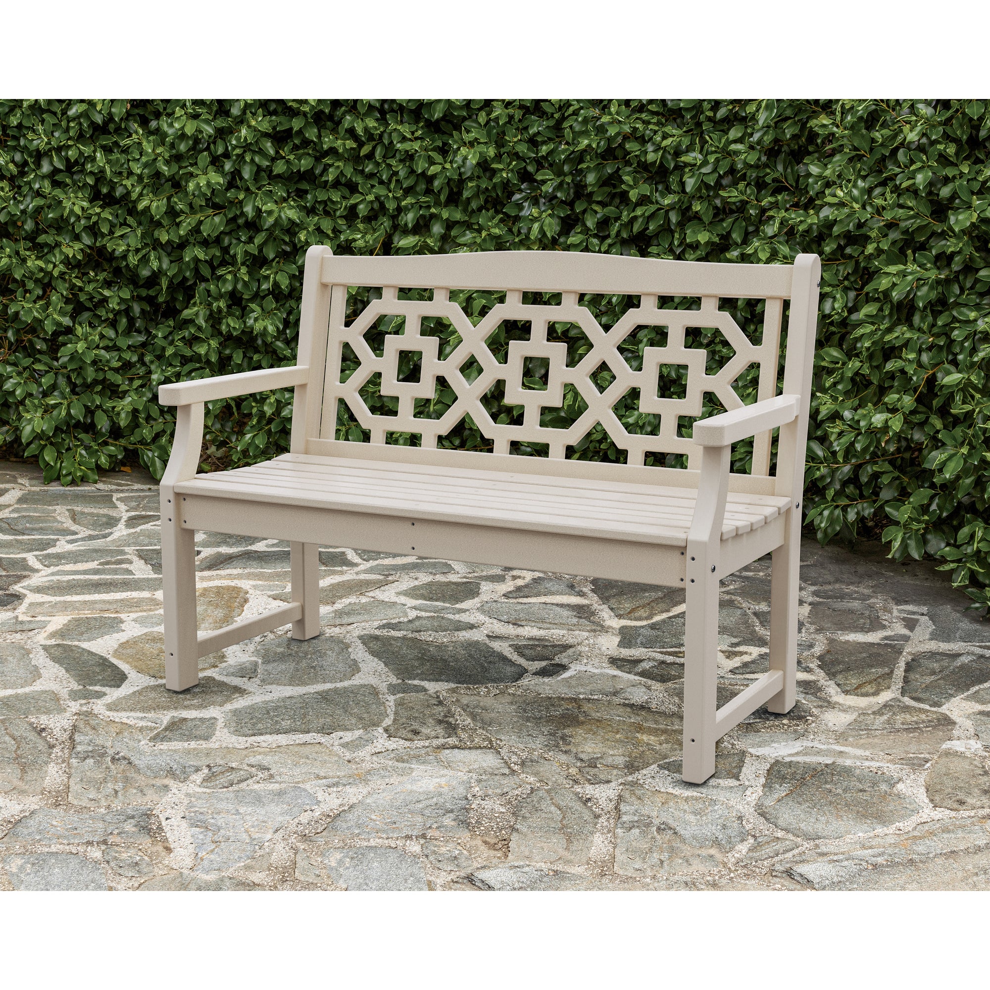 A light-colored POLYWOOD Chinoiserie garden bench sitting on stone paving outdoors.