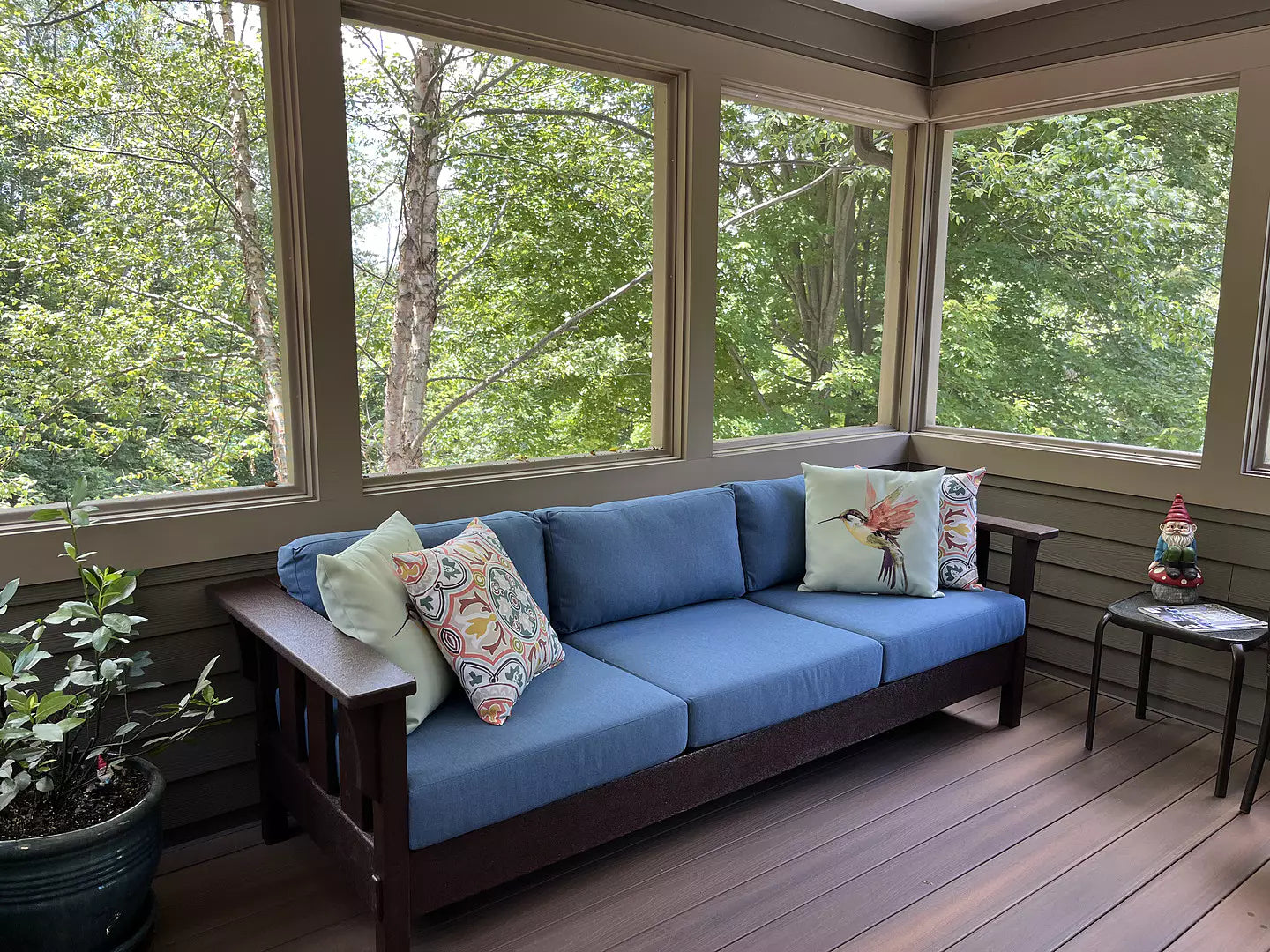 A POLYWOOD Acadia Deep Seating Sofa in Mahogany and Sky Blue is in a three season room with large windows overlooking trees.