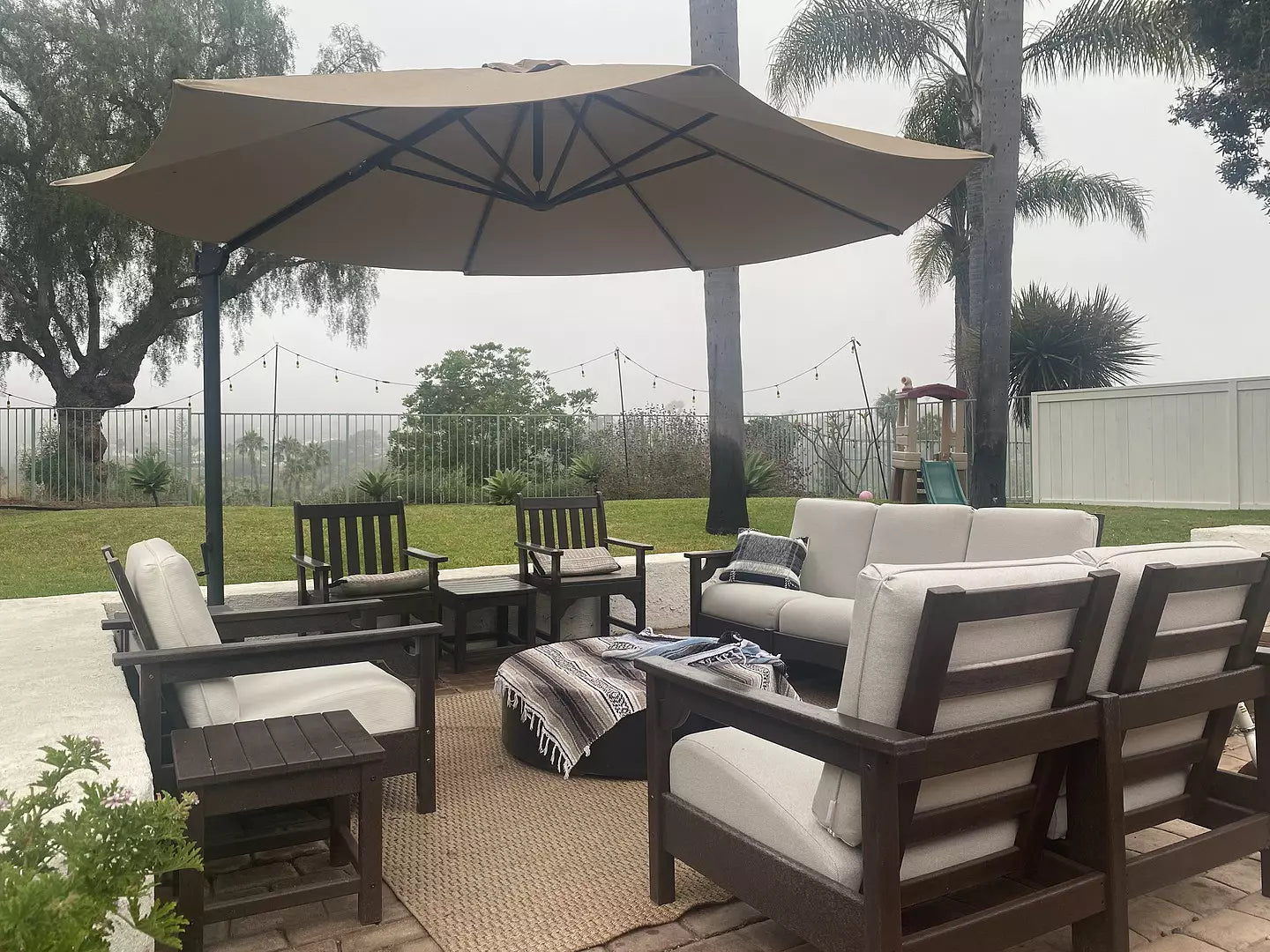 Assorted POLYWOOD Traditional Garden and Club seating in Mahogany and Dune Burlap sit beneath an umbrella on a brick patio.