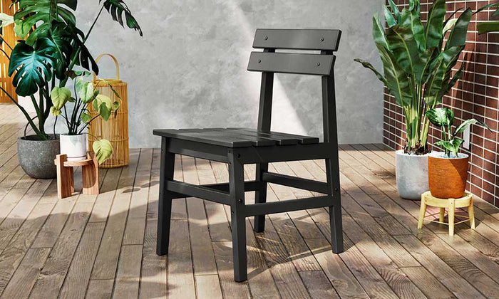 Black POLYWOOD Modern Studio dining chair, displayed on a wooden deck with a variety of plants and in front of a concrete wall