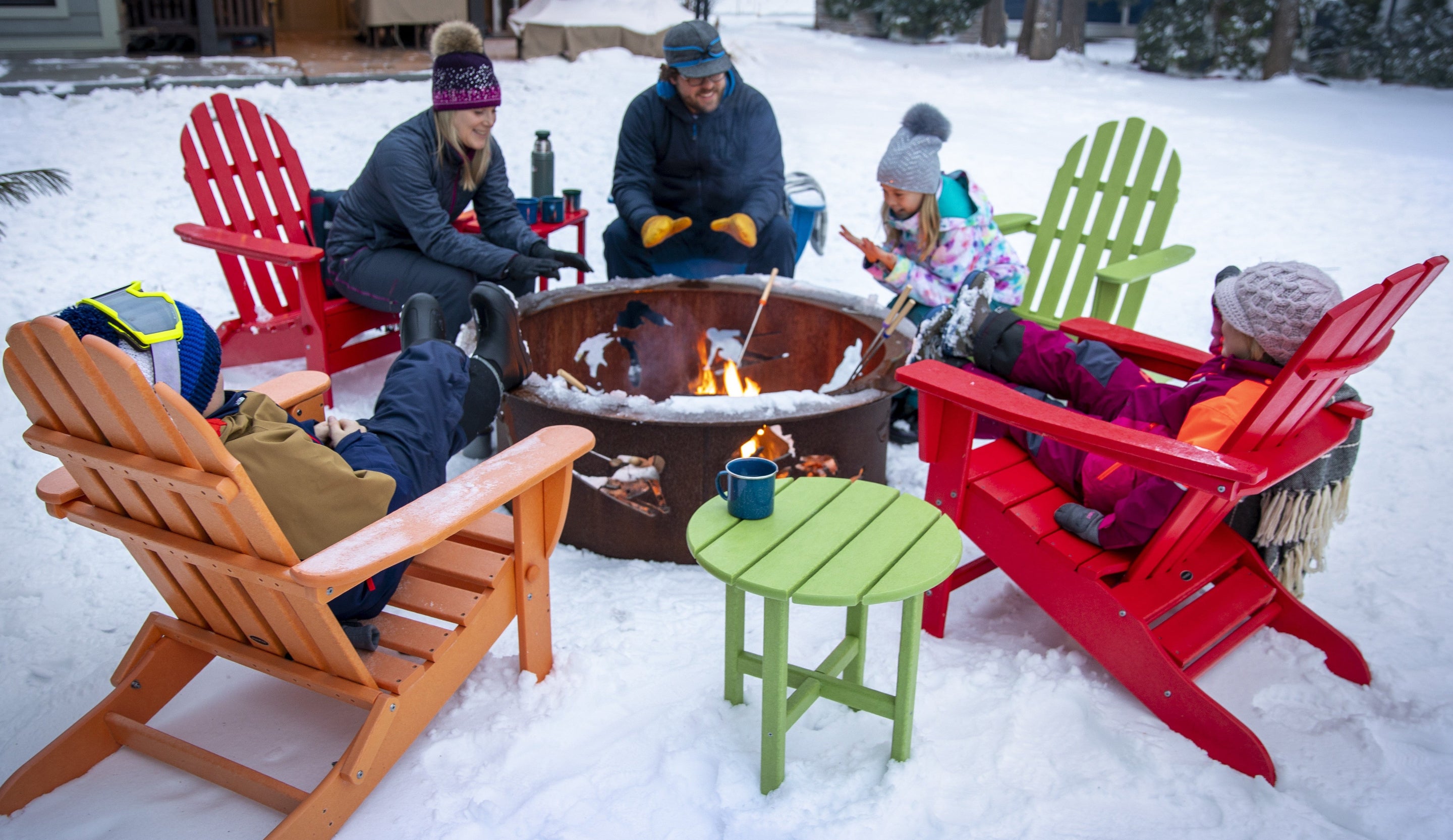 People gathered around a fire pit in a snowy outdoor setting with colorful POLYWOOD Adirondack chairs.