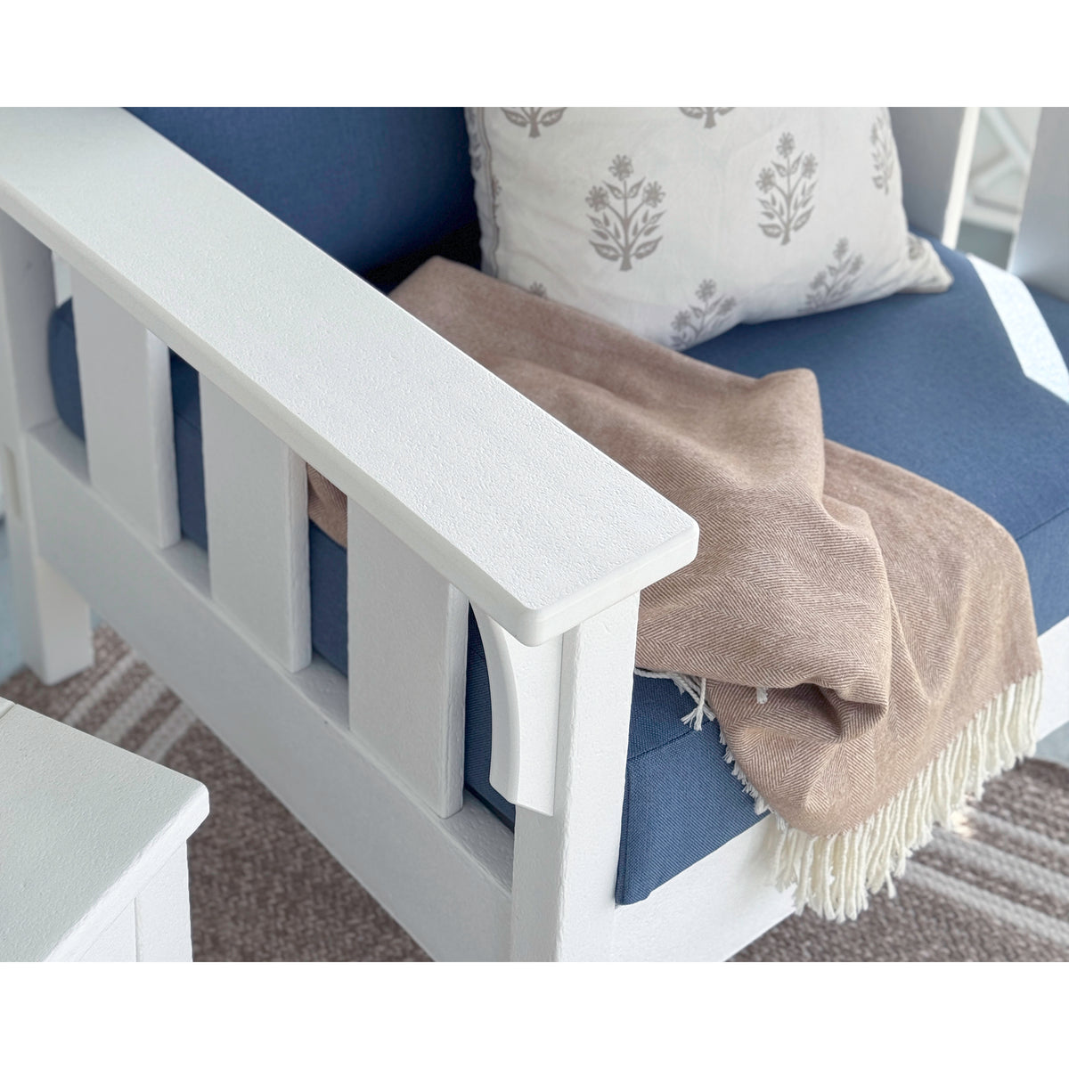 armrest of white outdoor chair with blue cushion and beige throw