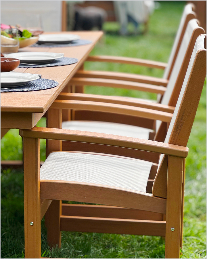 Brown POLYWOOD Coastal Dining Chairs with white sling seats line a wood-look dining table set with plates and placemats on a lawn.