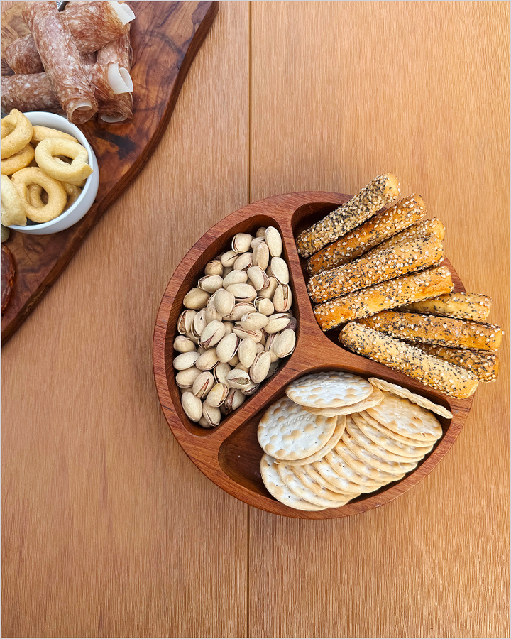 An overhead view of a brown POLYWOOD dining table holds a wooden snack tray with pistachios, crackers, and breadsticks.