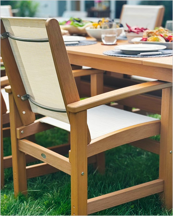 A tan POLYWOOD Coastal Dining Chair with a white sling seat sits at a dining table set for an outdoor meal.